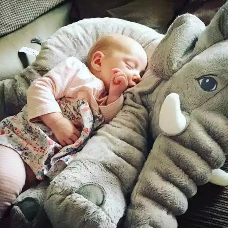 Baby sleeping next to a large plush elephant toy