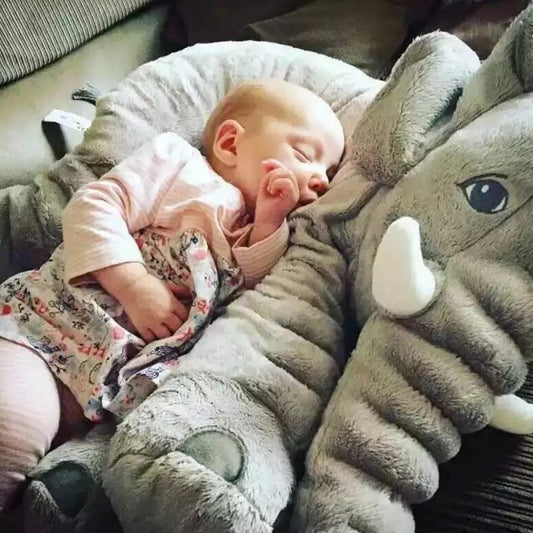 Baby sleeping next to a large plush elephant toy