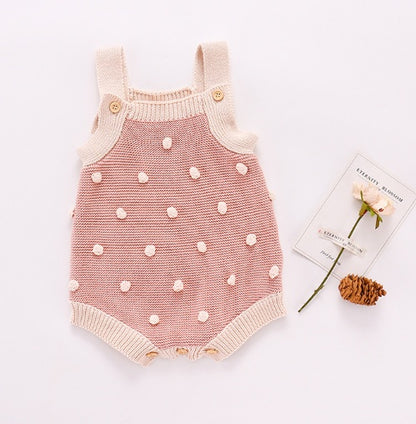 Pink polka dot baby romper on a white background with a small card and flower decoration.
