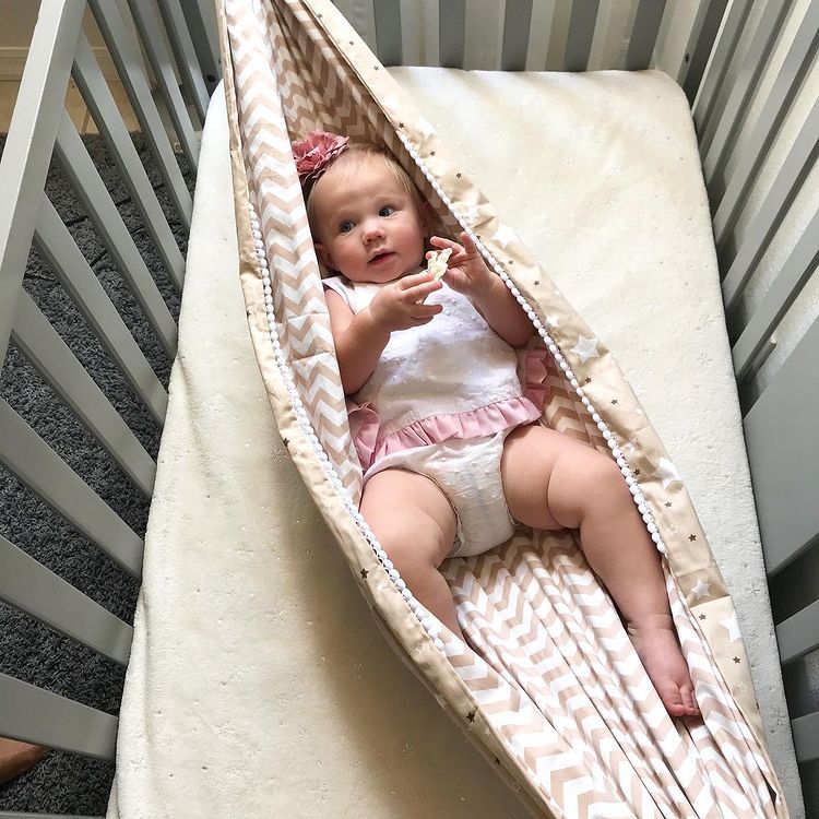 Baby sitting in a hammock attached to a crib
